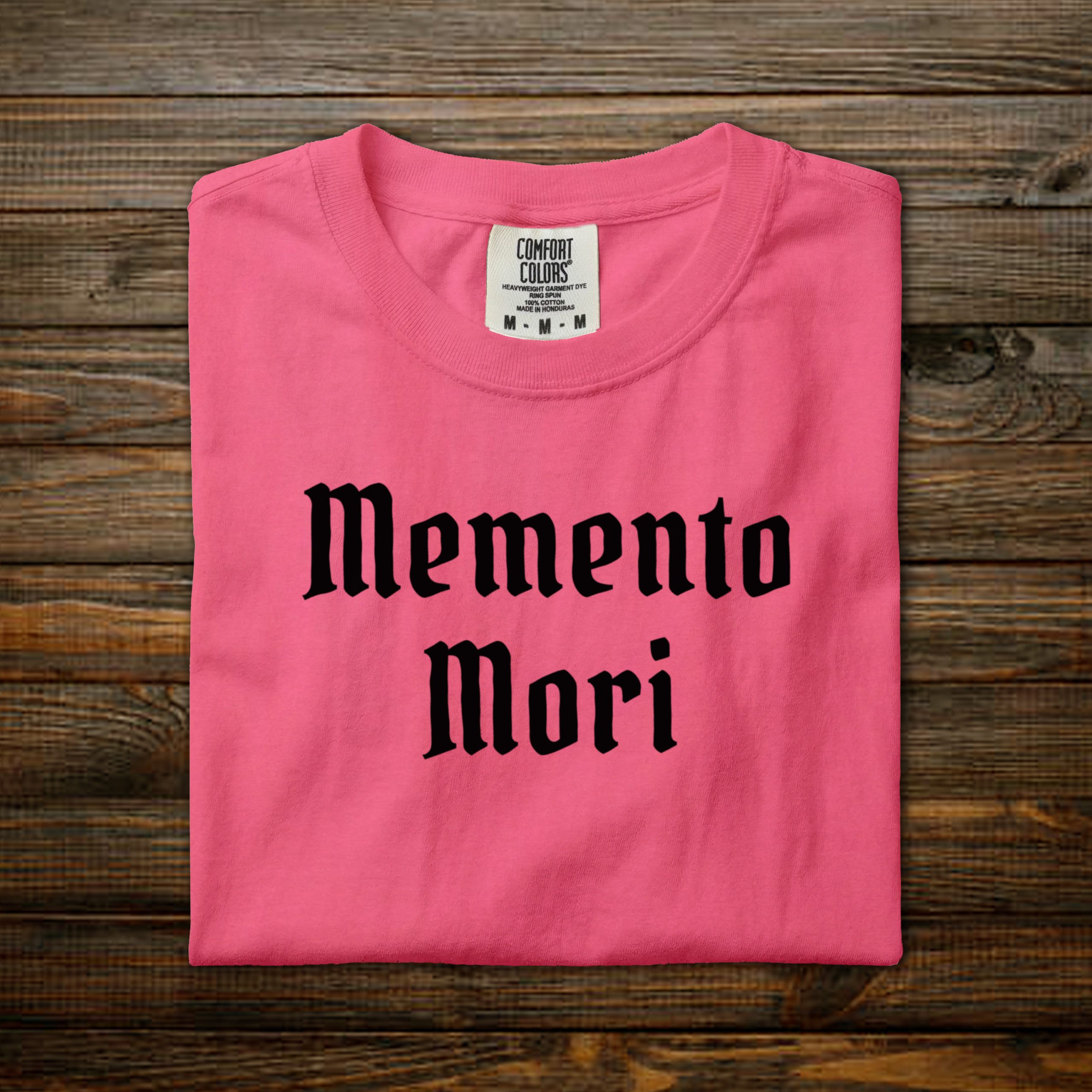 Memento Mori Comfort Colors tee with black old English lettering, folded on wood background