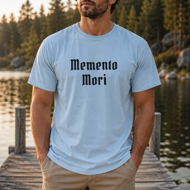 Memento Mori Comfort Colors tee with black old English lettering, folded on wood background